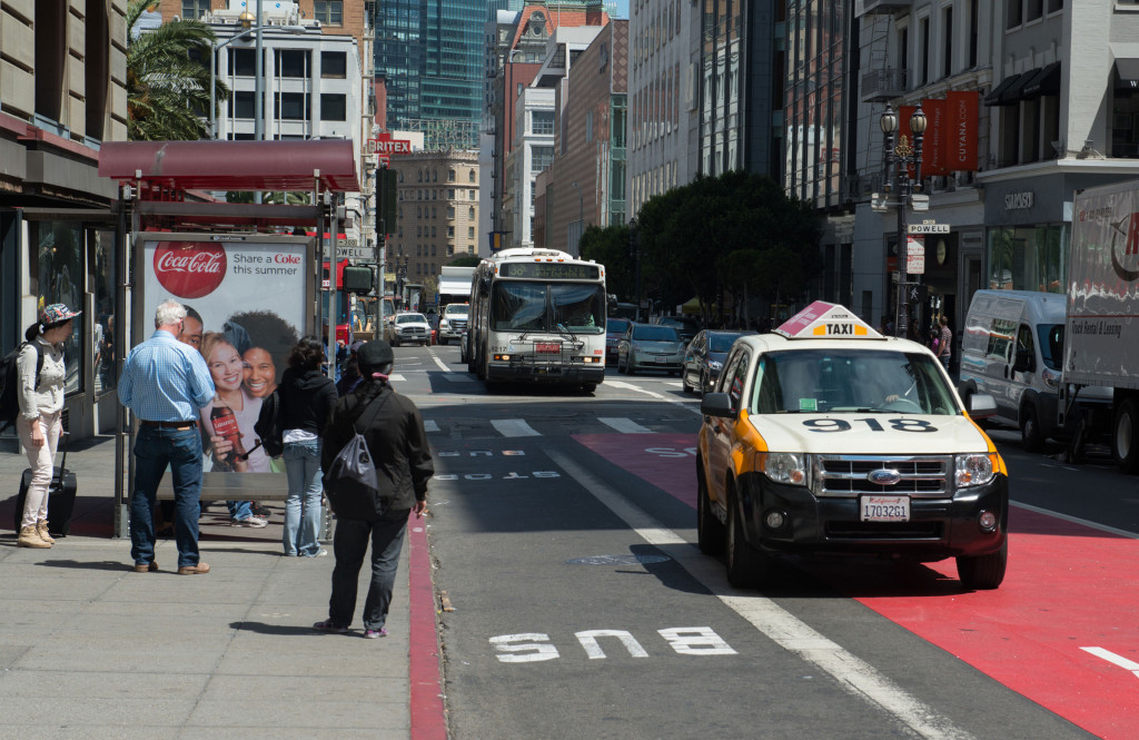 Taxi and Muni bus driving. Pedestrians waiting at bus stop.